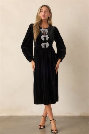 A chic black velvet midi dress with long sleeves and a mock neck, paired with pointed-toe heels and silver accessories for a winter wedding look.